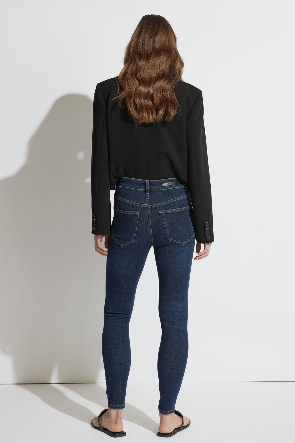 Woman modeling dark indigo high-rise skinny jeans paired with a tailored black blazer and casual sandals