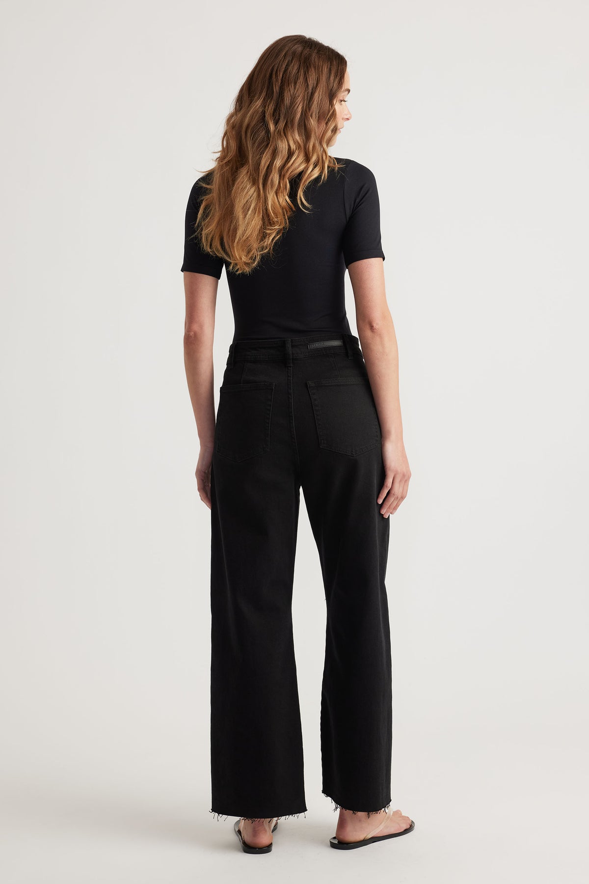 Woman wearing a fitted black tee paired with high-rise wide-leg black jeans featuring raw hem detailing.