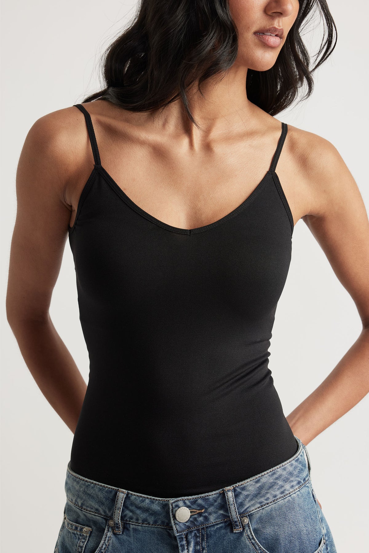 Woman wearing a fitted black thin-strap tank top paired with casual light-wash denim jeans, cropped at the waist.