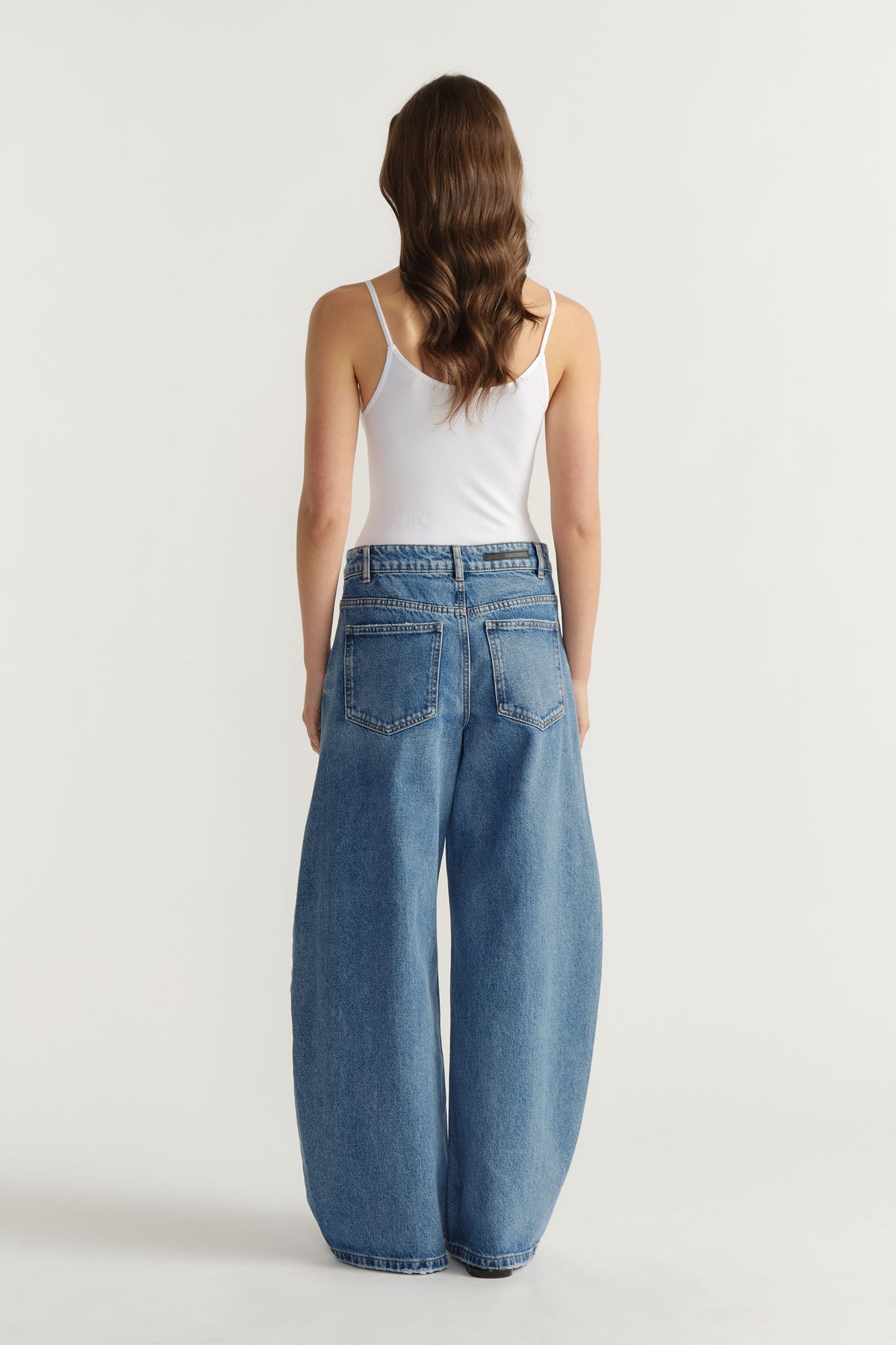 Back view of woman wearing light blue wide-leg jeans paired with a white seamless thin strap tank top
