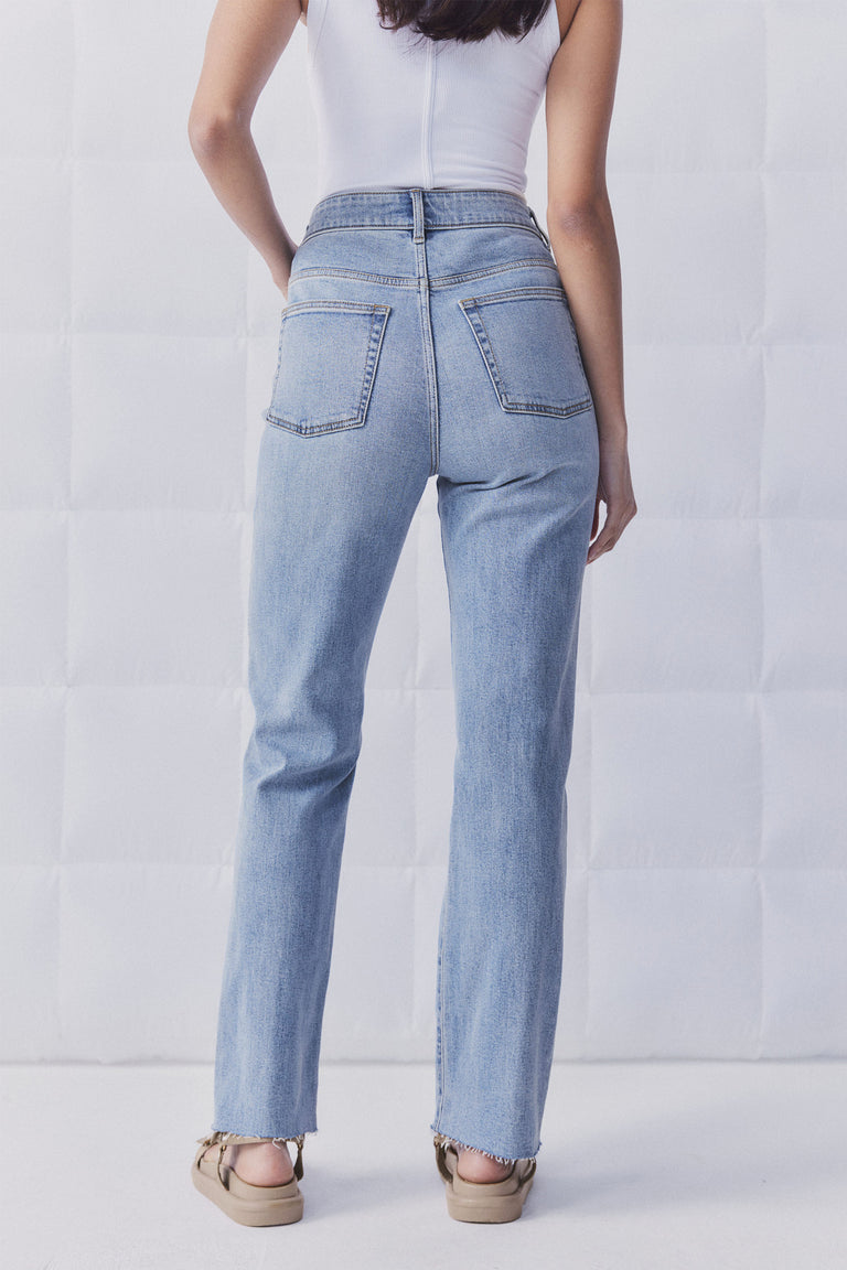 Woman wearing light blue straight leg denim jeans with a high waist and raw hem paired with neutral sandals