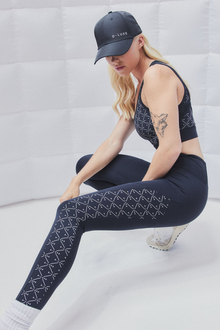 Woman wearing black high rise leggings with a D-Luxe monogram print along the sides