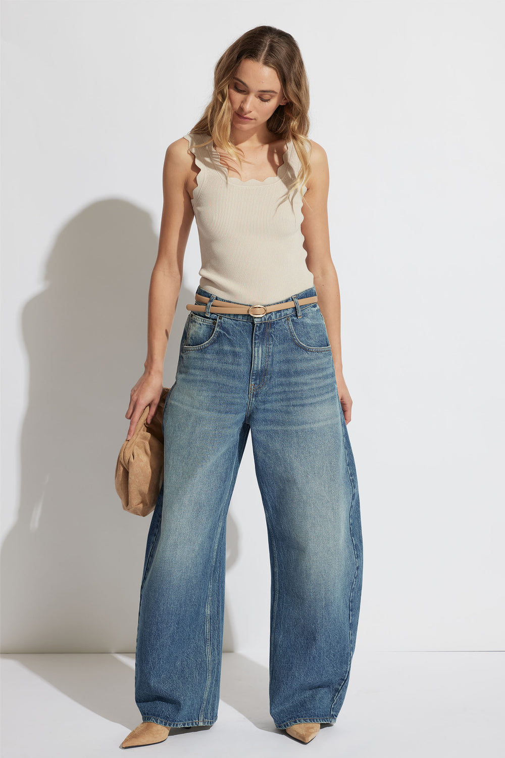 Woman wearing a beige scallop edge tank with wide straps paired with loose-fitting blue denim jeans and tan heels.