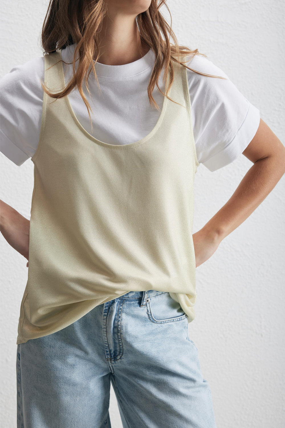Woman wearing a cream metallic tank over a white tee, styled with relaxed blue jeans