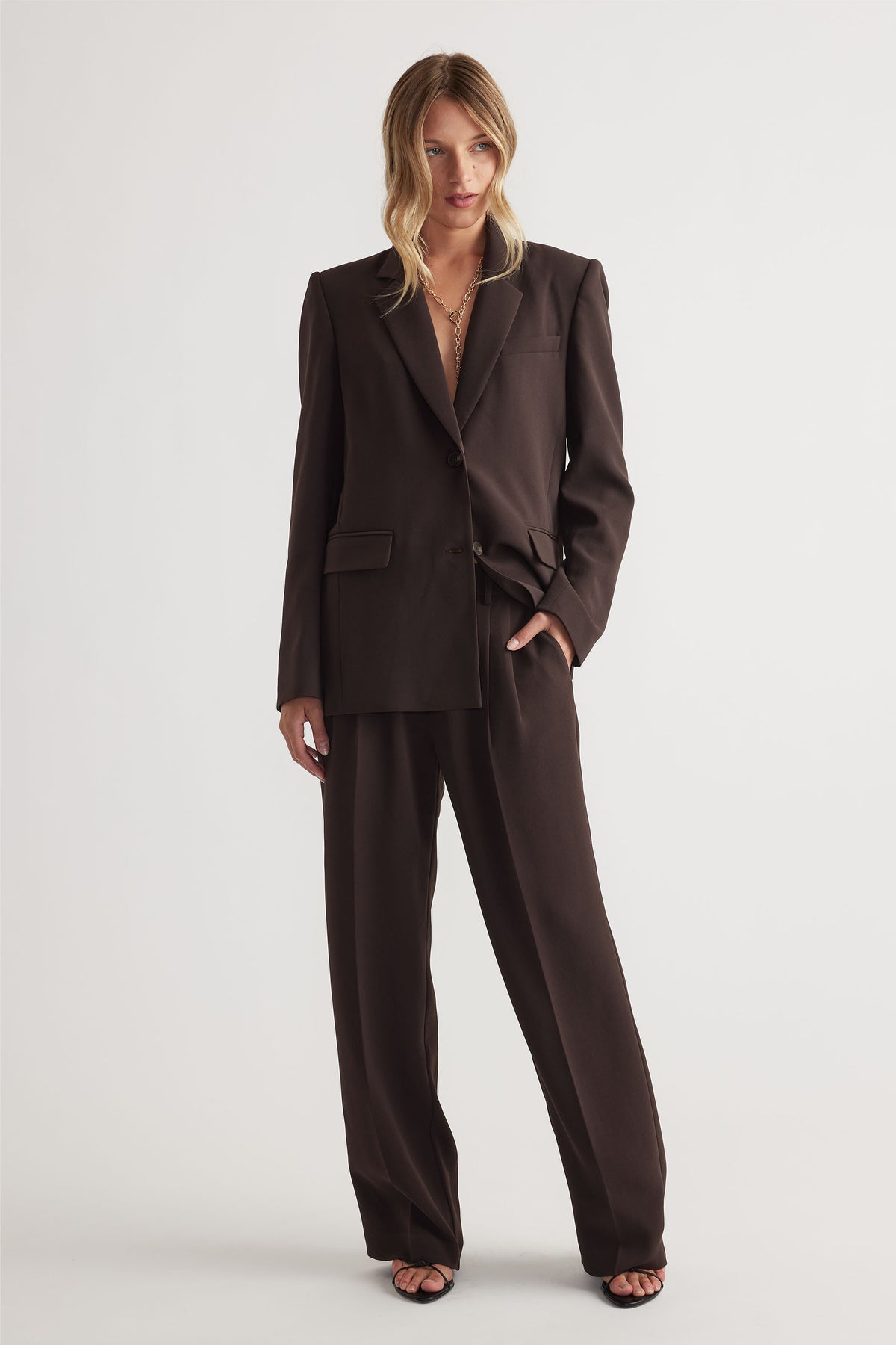 Woman wearing a dark brown tailored blazer and matching wide-leg pants styled for chic, polished office wear.