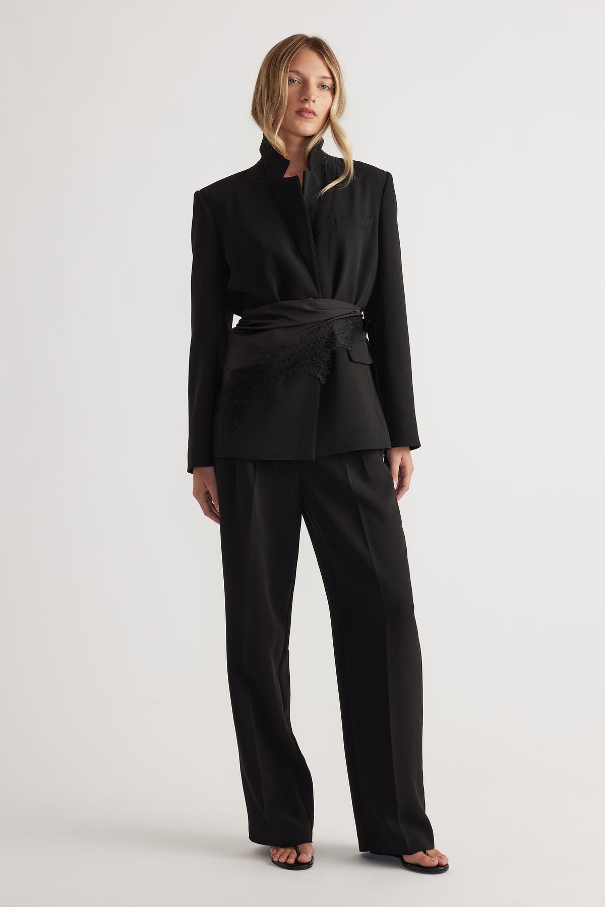 Woman wearing tailored black pants and a matching structured blazer cinched at the waist with a textured belt