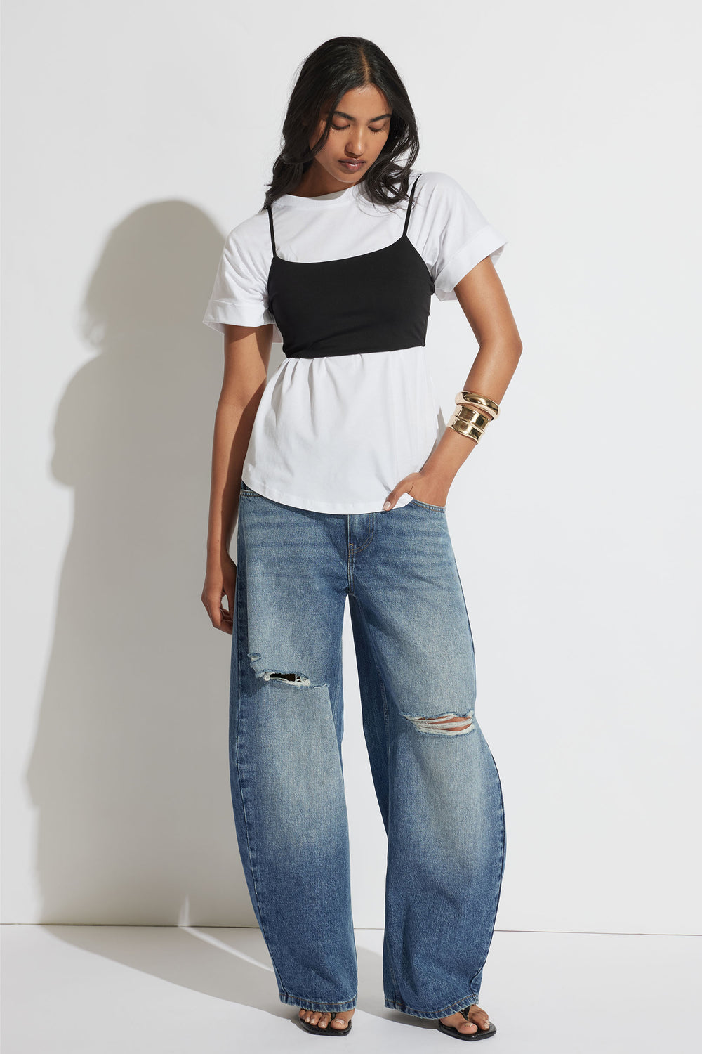 Woman wearing a black fitted crop top over a white T shirt with relaxed ripped blue jeans