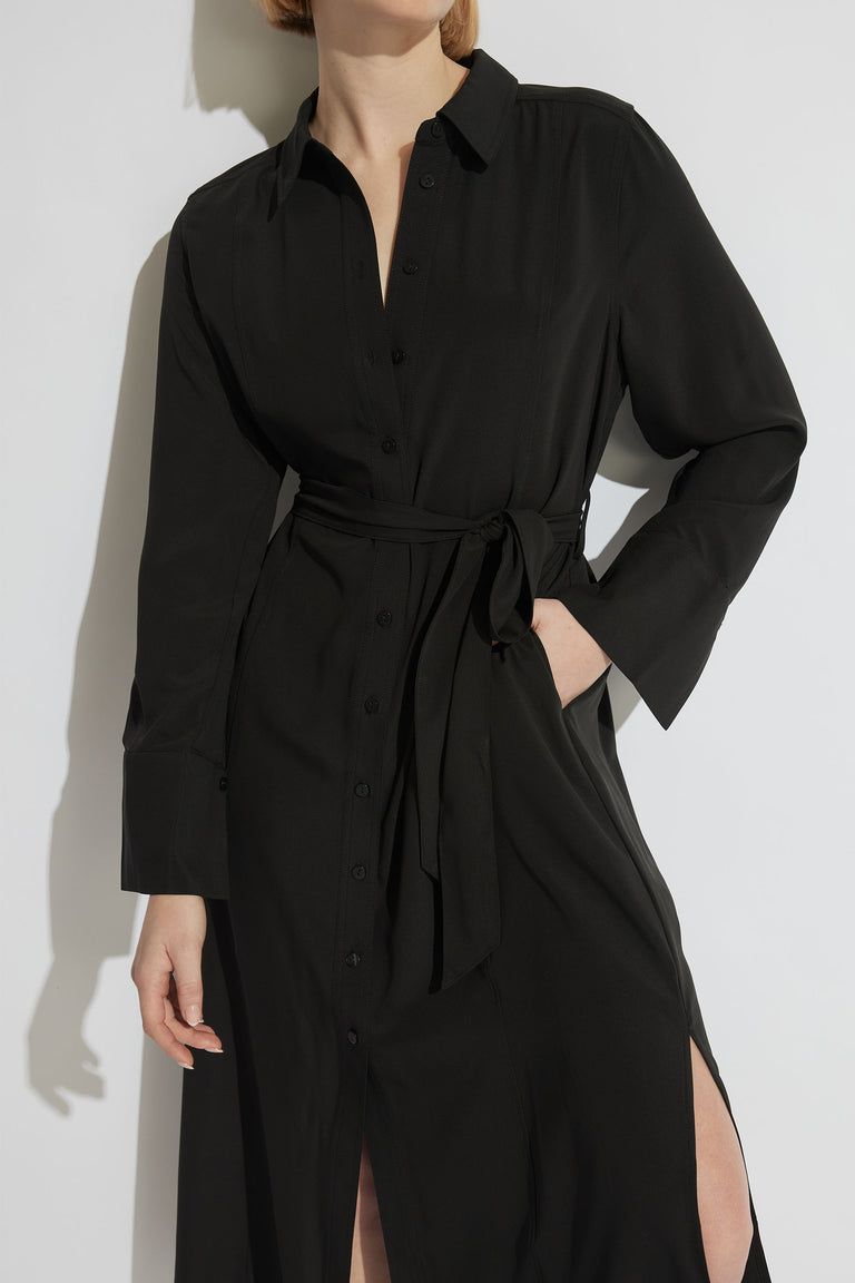 Woman wearing a black collared maxi dress with long sleeves, button front, waist ties and side splits