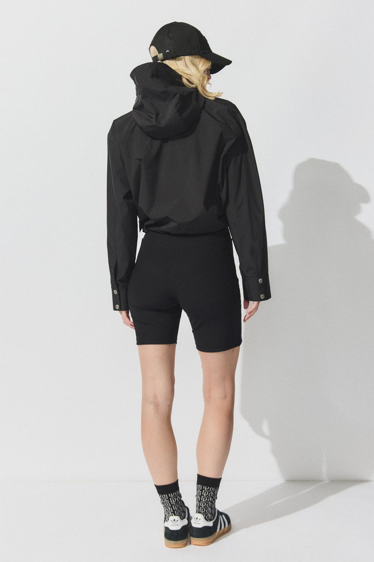 Back view portrait of model wearing black D-Luxe Cropped Spray Jacket with hood, gallery image 3, size 1880x2820 pixels.
