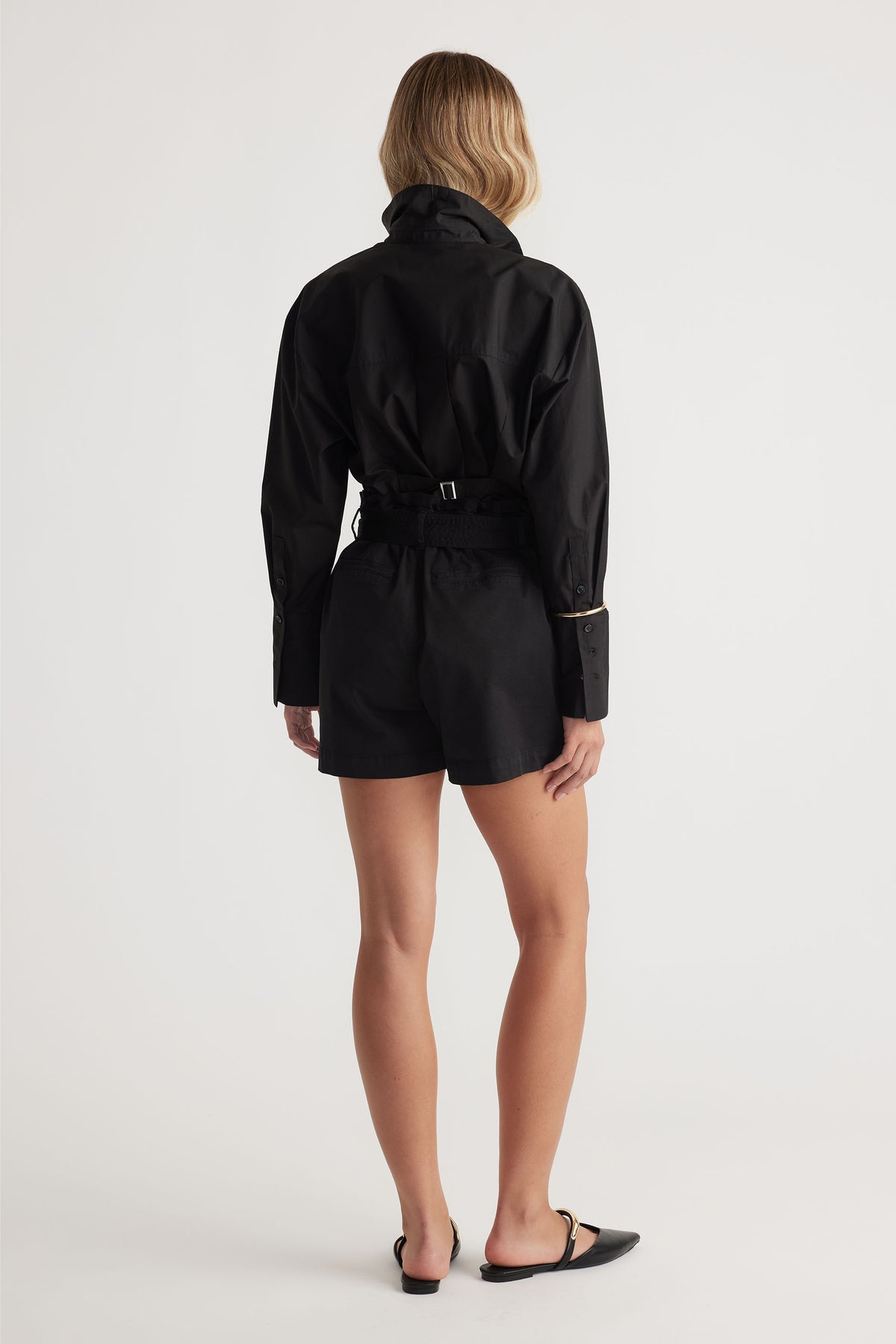 Rear view of a woman wearing black tailored shorts paired with a long-sleeve fitted black shirt and pointed flats