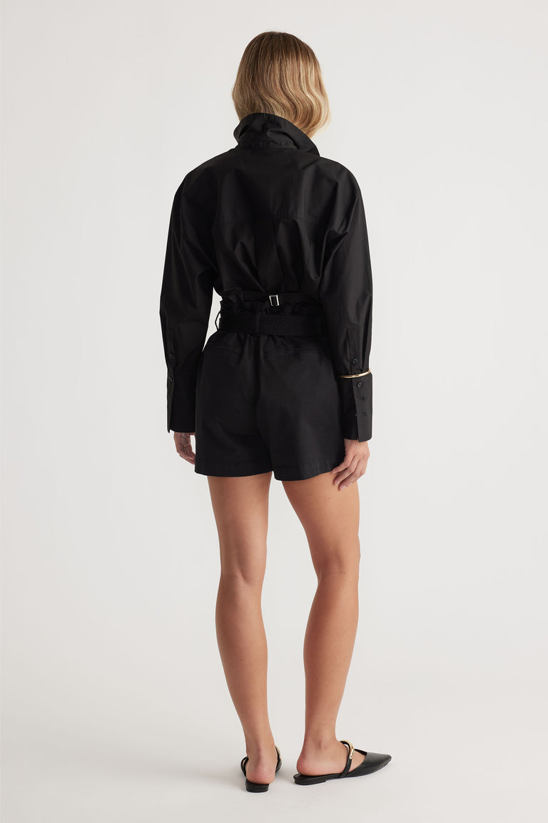 Rear view of a woman wearing black tailored shorts paired with a long-sleeve fitted black shirt and pointed flats