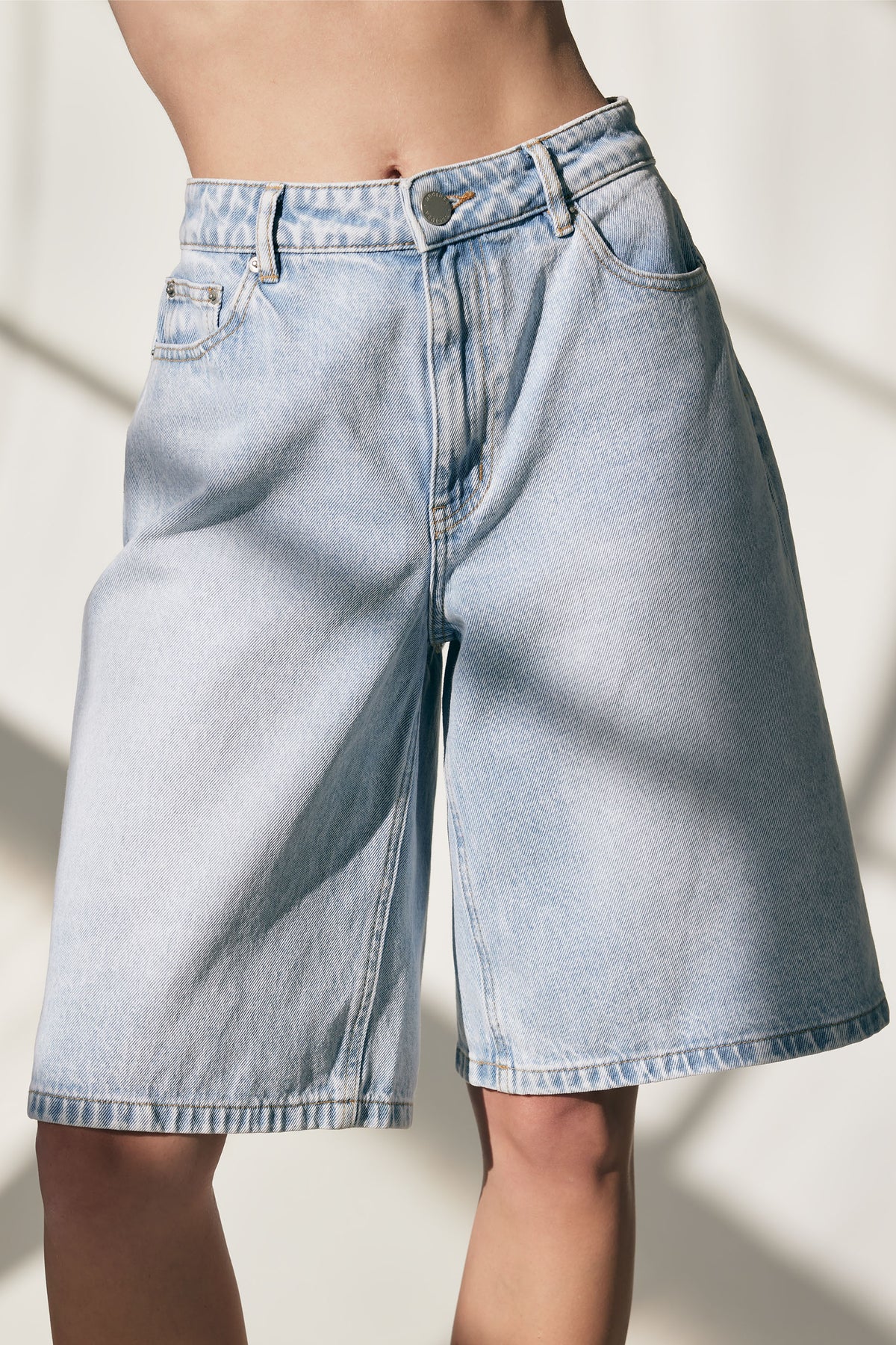 Light wash longline denim shorts with a relaxed fit and classic five-pocket styling for casual summer wear.