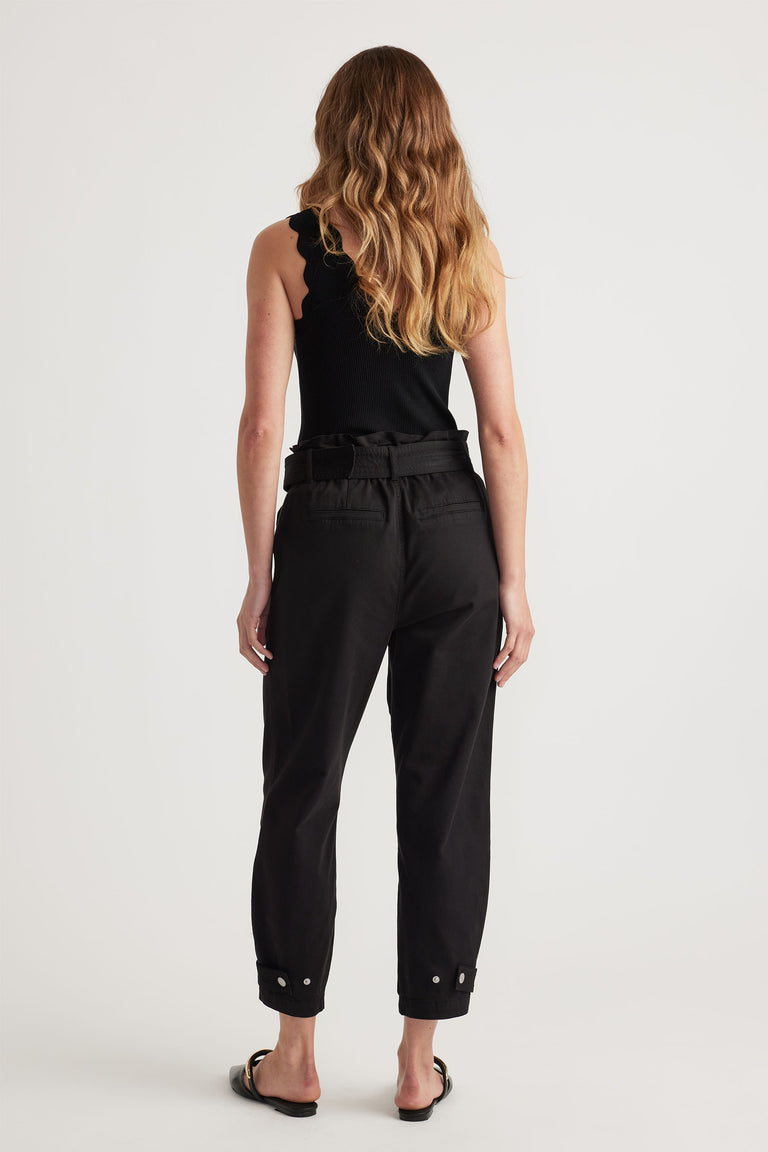 Back view of woman wearing black belted pull-on pants with cuffed ankles paired with a scalloped black tank top