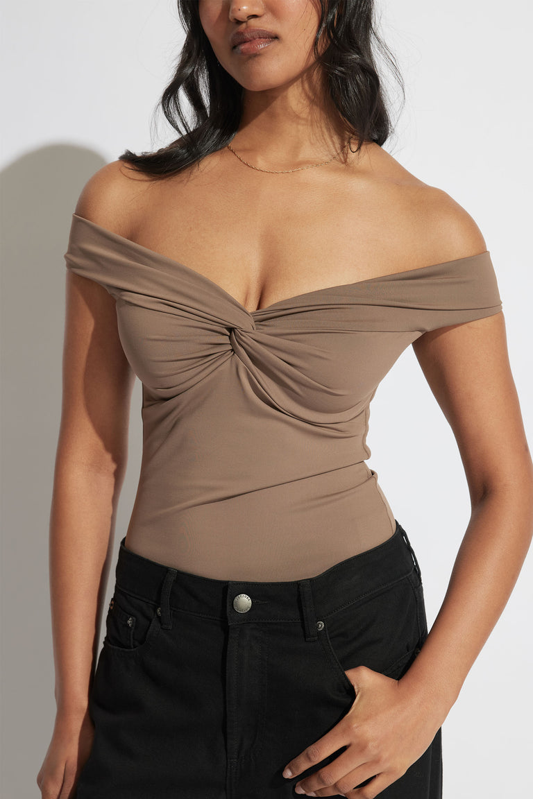 Woman wearing a cappuccino off-shoulder twist top paired with high-waisted black jeans in a minimalist setting.