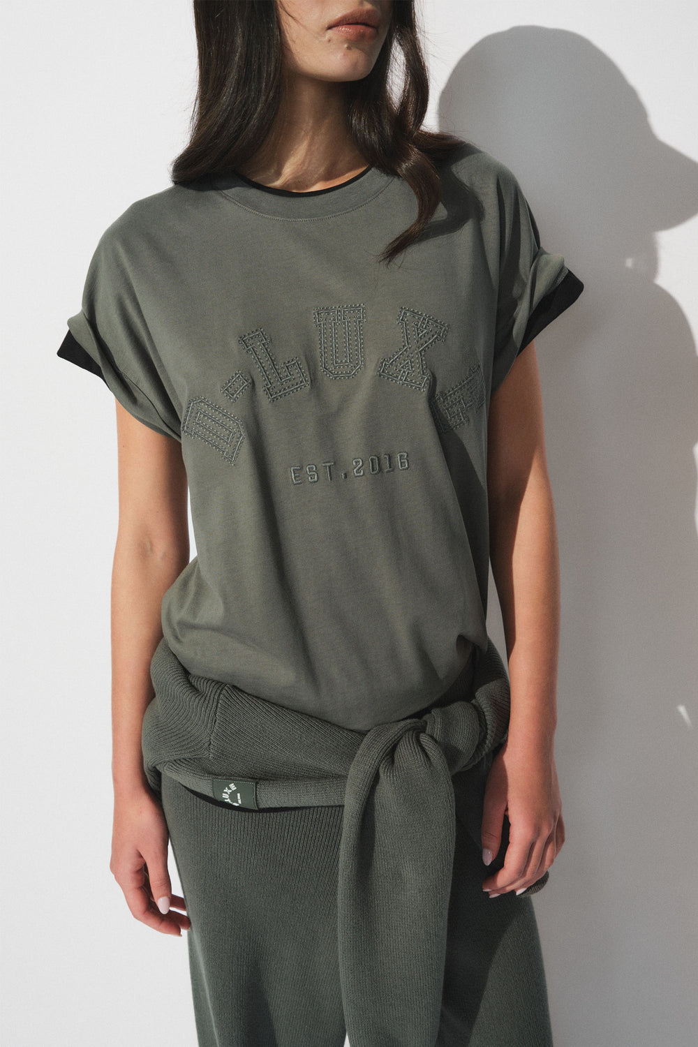 Woman wearing an olive green oversized tee with tonal D Luxe chest branding and rolled sleeves