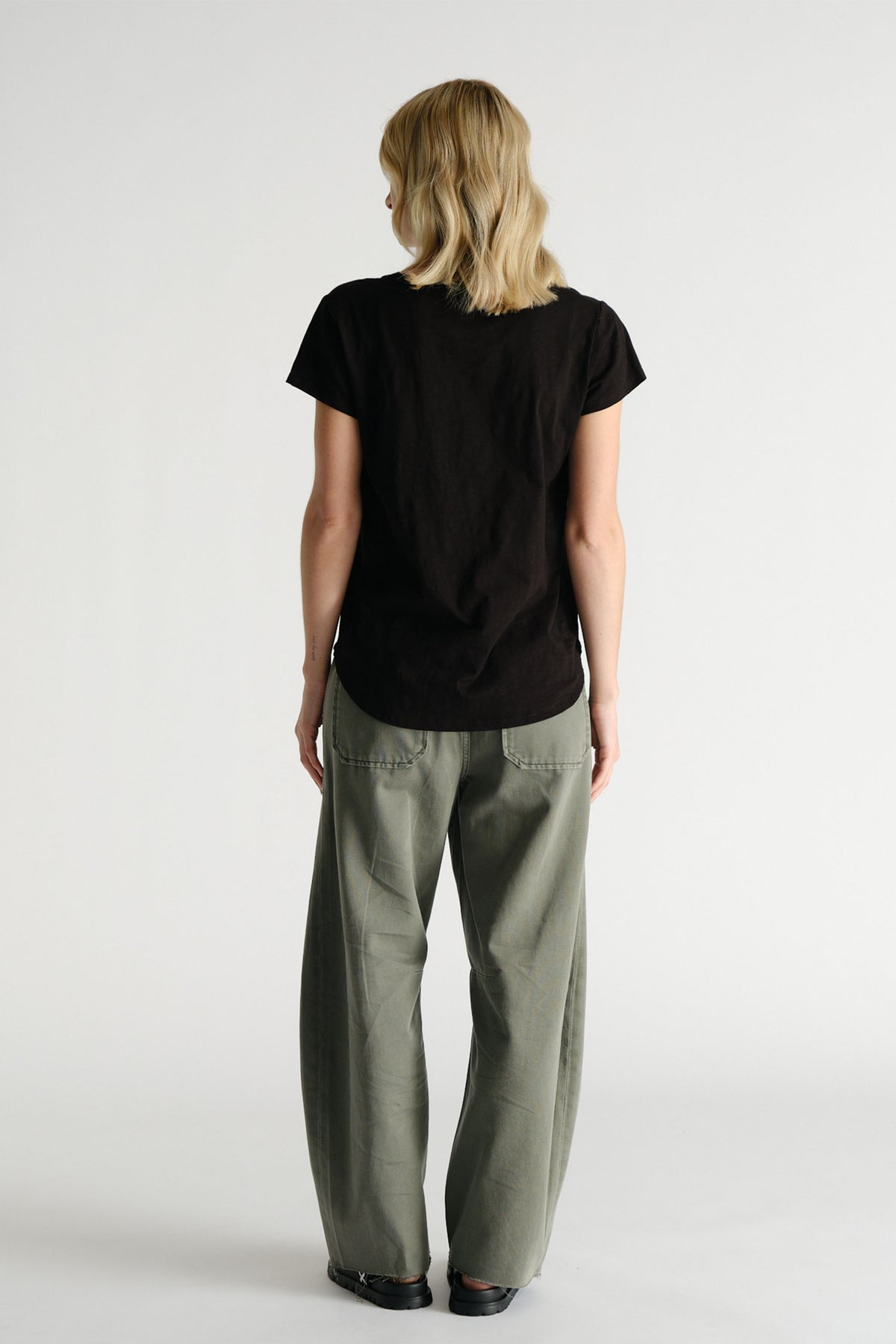 Woman wearing a relaxed black D-Luxe Slub Tee paired with loose olive green pants for effortless casual style