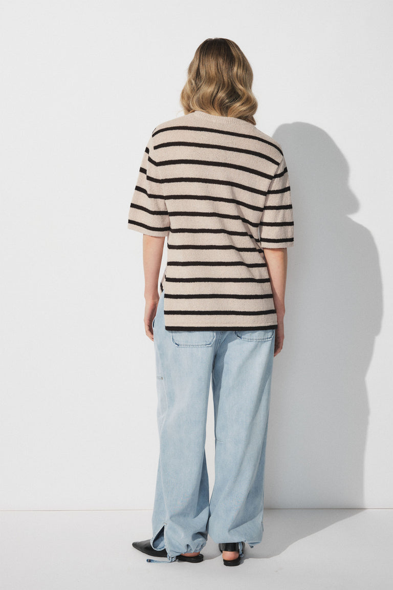 Woman wearing a beige knit top with black stripes paired with light wash wide-leg denim joggers in a relaxed pose