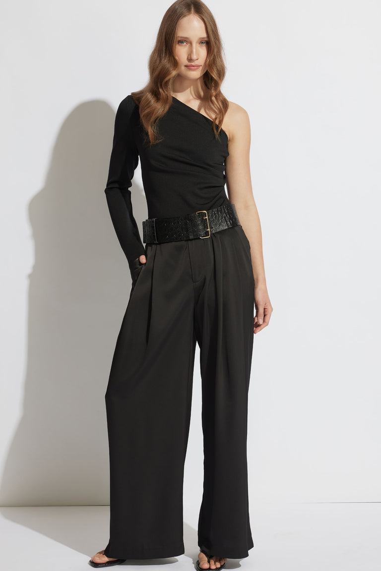 Woman wearing a black one-shoulder top with one long sleeve paired with high-waisted wide-leg pants and a textured belt