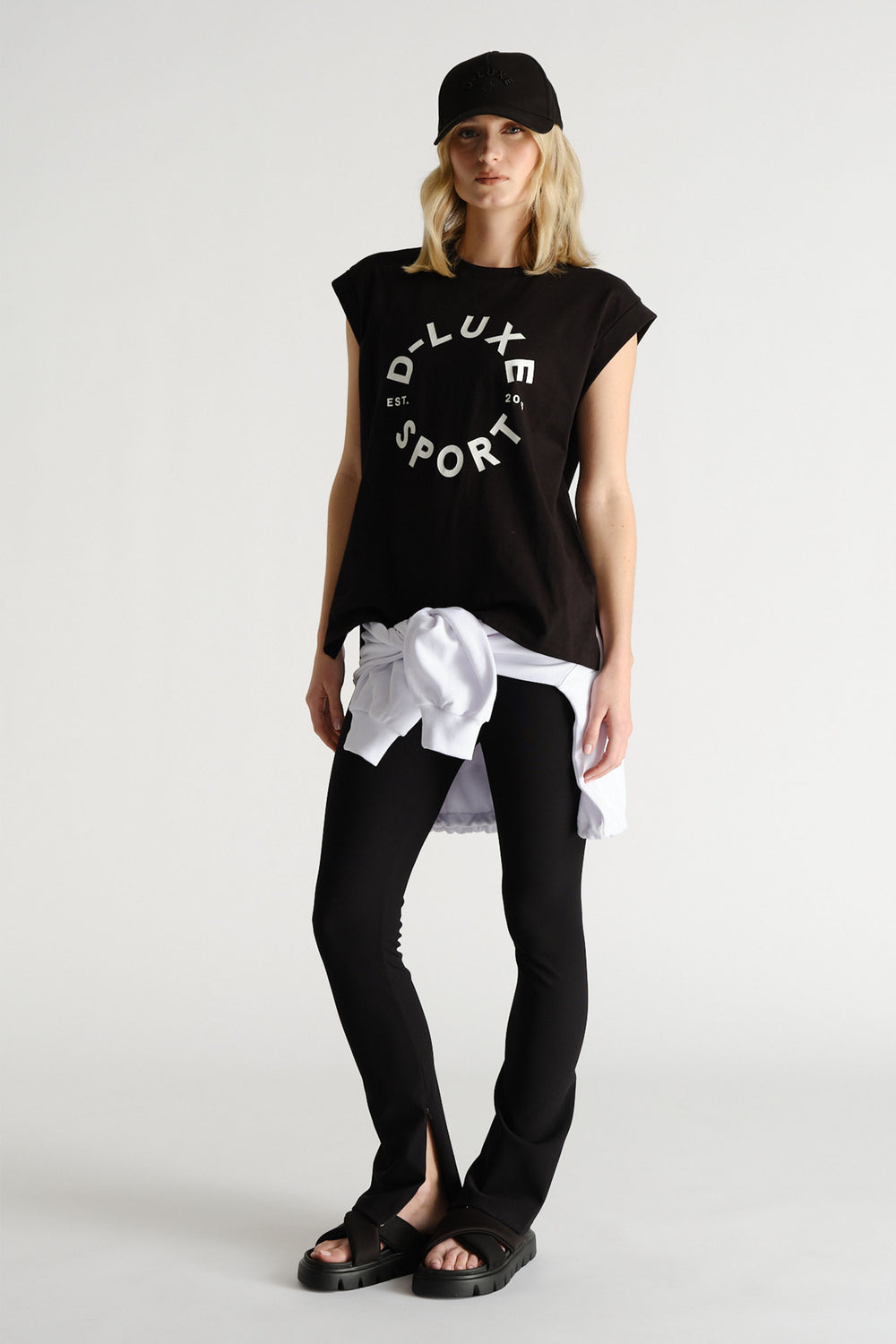 Woman wearing a black sleeveless tank with graphic print, paired with black leggings and a white sweatshirt tied at the waist