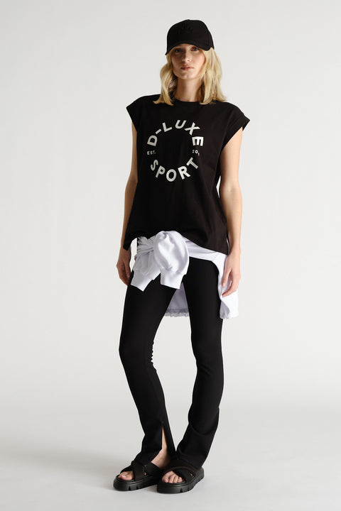 Woman wearing a black sleeveless tank with graphic print, paired with black leggings and a white sweatshirt tied at the waist