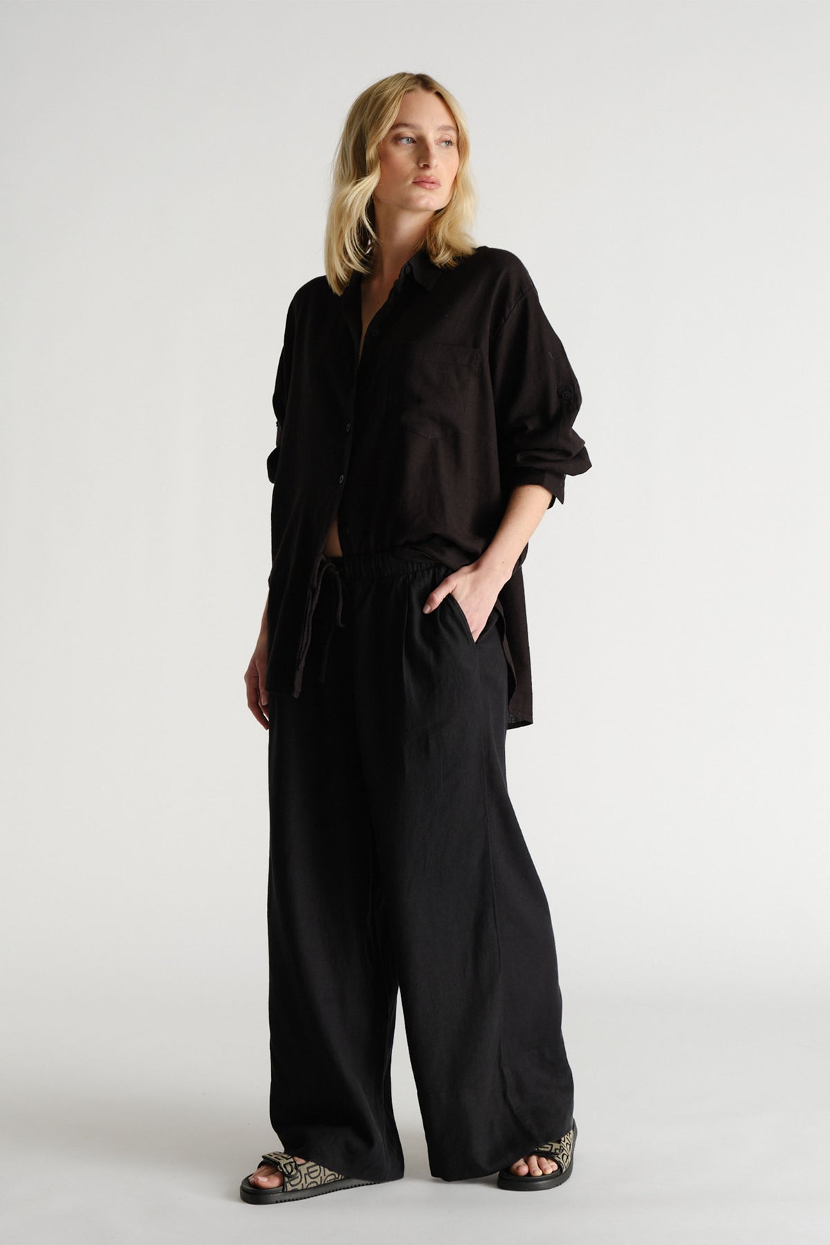 Woman wearing black D-Luxe Linen Blend LS Shirt in portrait, gallery position 2, styled with relaxed black pants and sandals