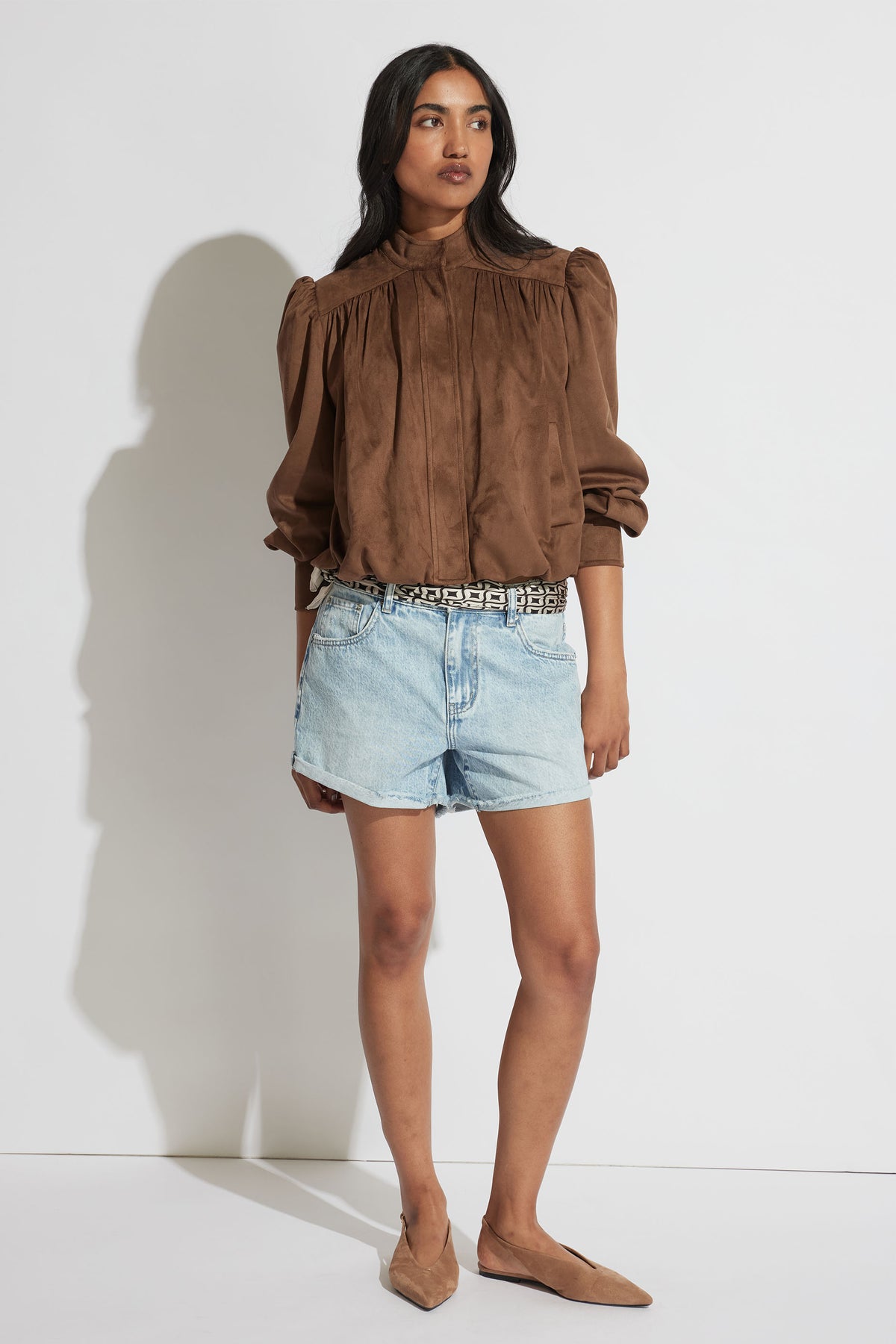Woman styled in a relaxed brown blouse with puff sleeves paired with rolled cuff light blue denim shorts and flats