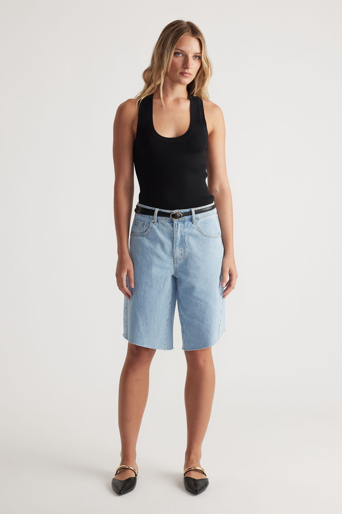 Woman wearing light wash denim shorts paired with a black tank top and pointed black flats for a casual look