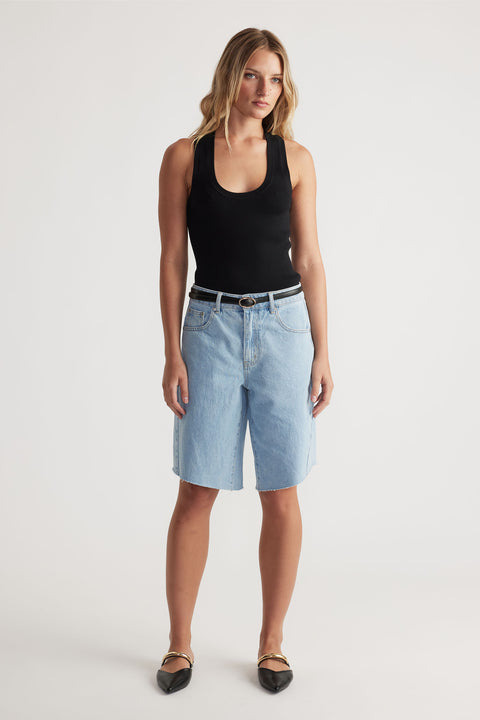 Woman wearing light wash denim shorts paired with a black tank top and pointed black flats for a casual look