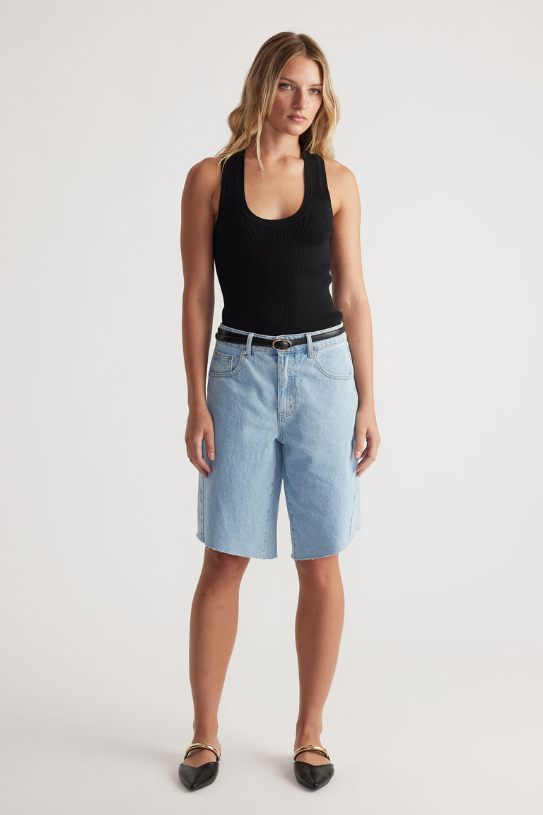 Woman wearing a fitted black racerback knit tank paired with light blue denim bermuda shorts and black pointed flats.