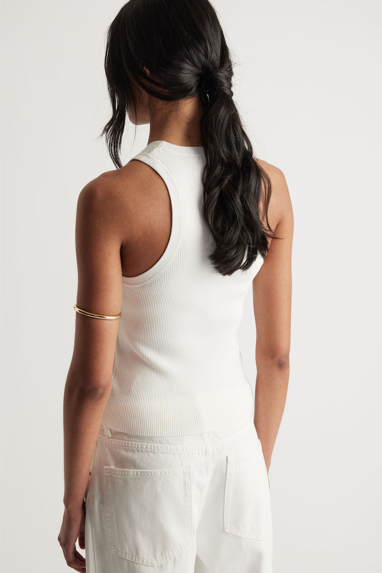 Back view of a woman wearing an ivory ribbed knit racerback tank paired with white high-waisted pants and a gold arm cuff.