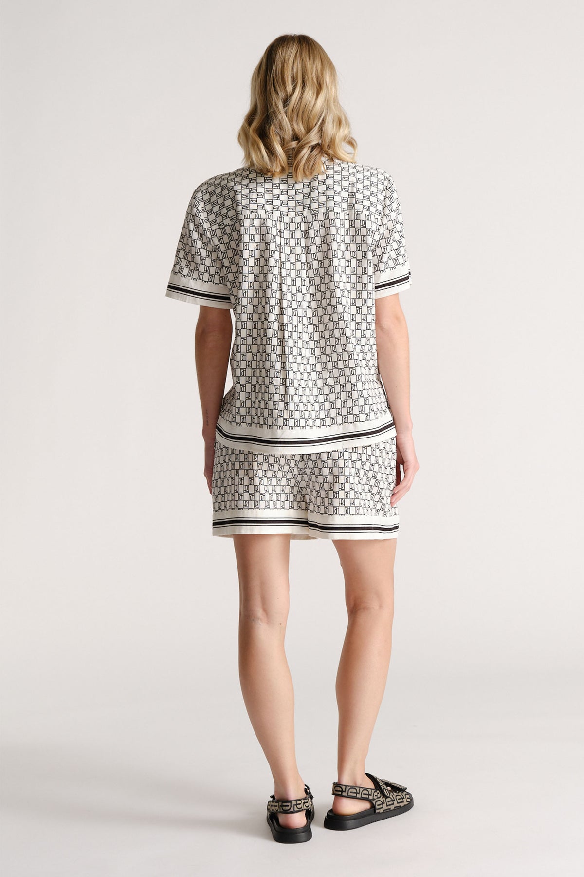 Woman wearing a patterned short-sleeve shirt and matching shorts with black and white striped trim, seen from behind.