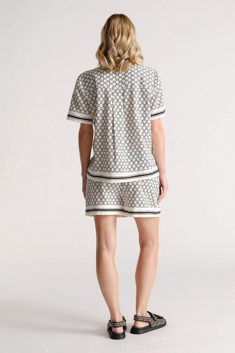 Woman wearing a patterned short-sleeve shirt and matching shorts with black and white striped trim, seen from behind.