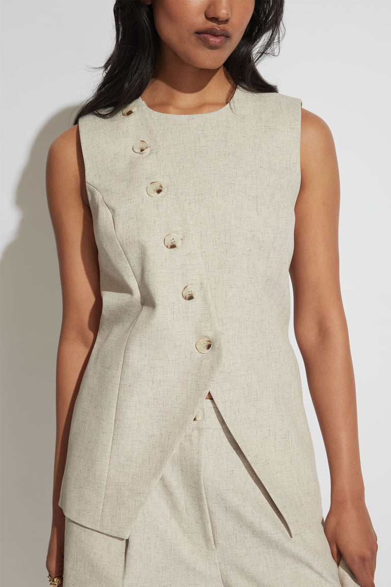 Woman wearing a beige longline sleeveless vest with a round neckline and asymmetrical button fastening