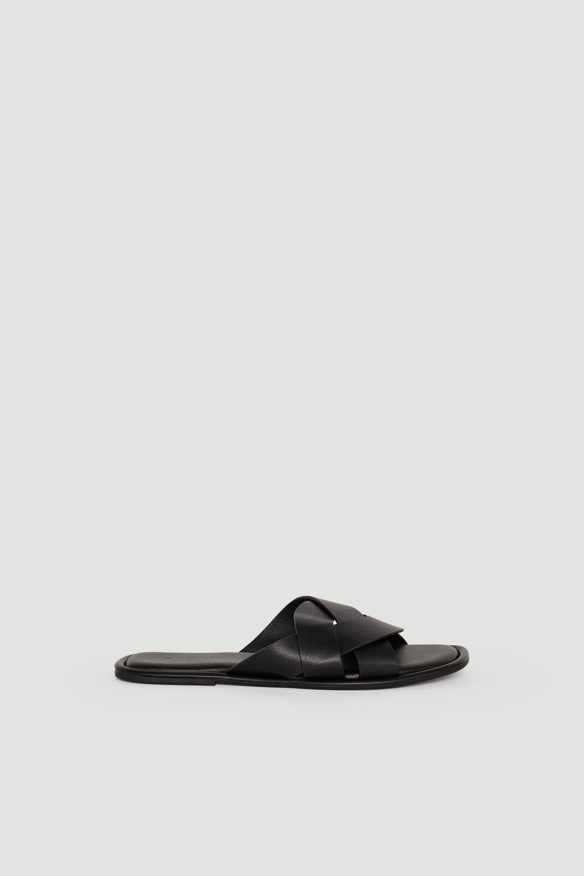 Black leather slide sandal with wide crossover straps and a flat sole, styled for effortless everyday wear.