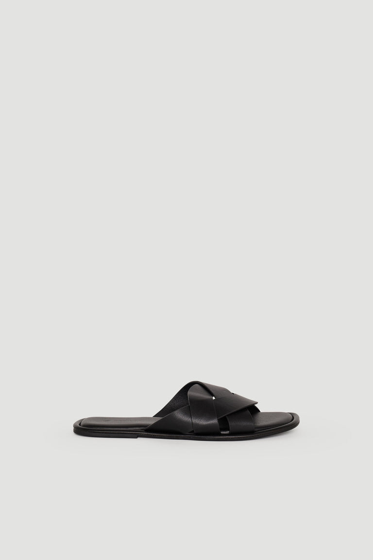 Black leather slide sandal with wide crossover straps and a flat sole, styled for effortless everyday wear.
