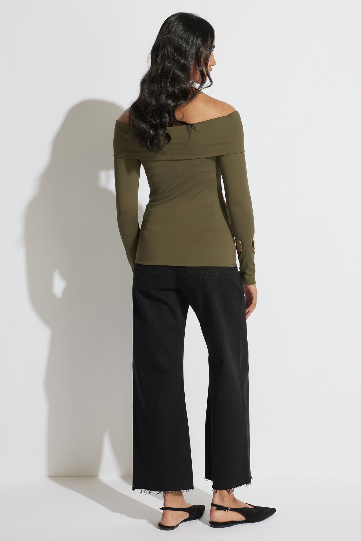 Woman seen from behind wearing an off-shoulder olive green long sleeve top paired with cropped black jeans and flats
