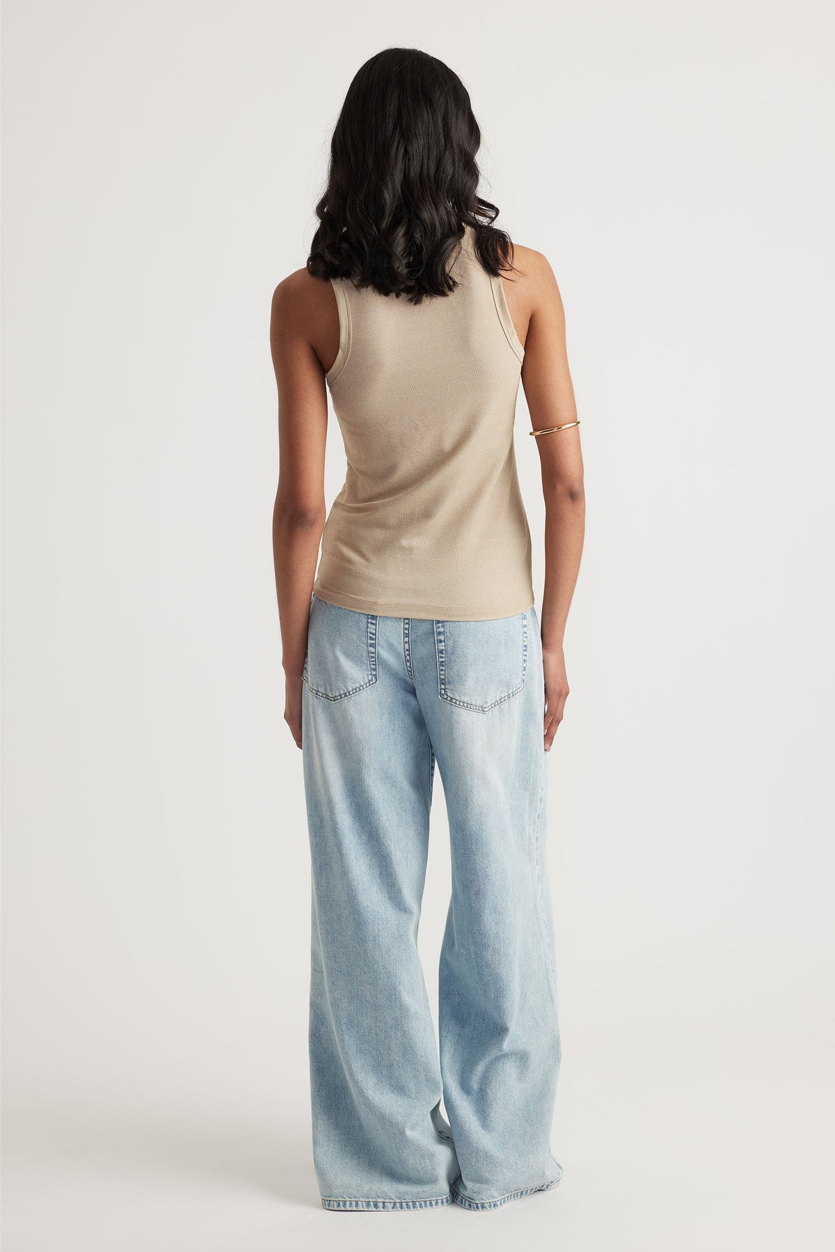 Woman wearing a neutral sleeveless tank top paired with relaxed light wash wide-leg denim jeans against a plain background.