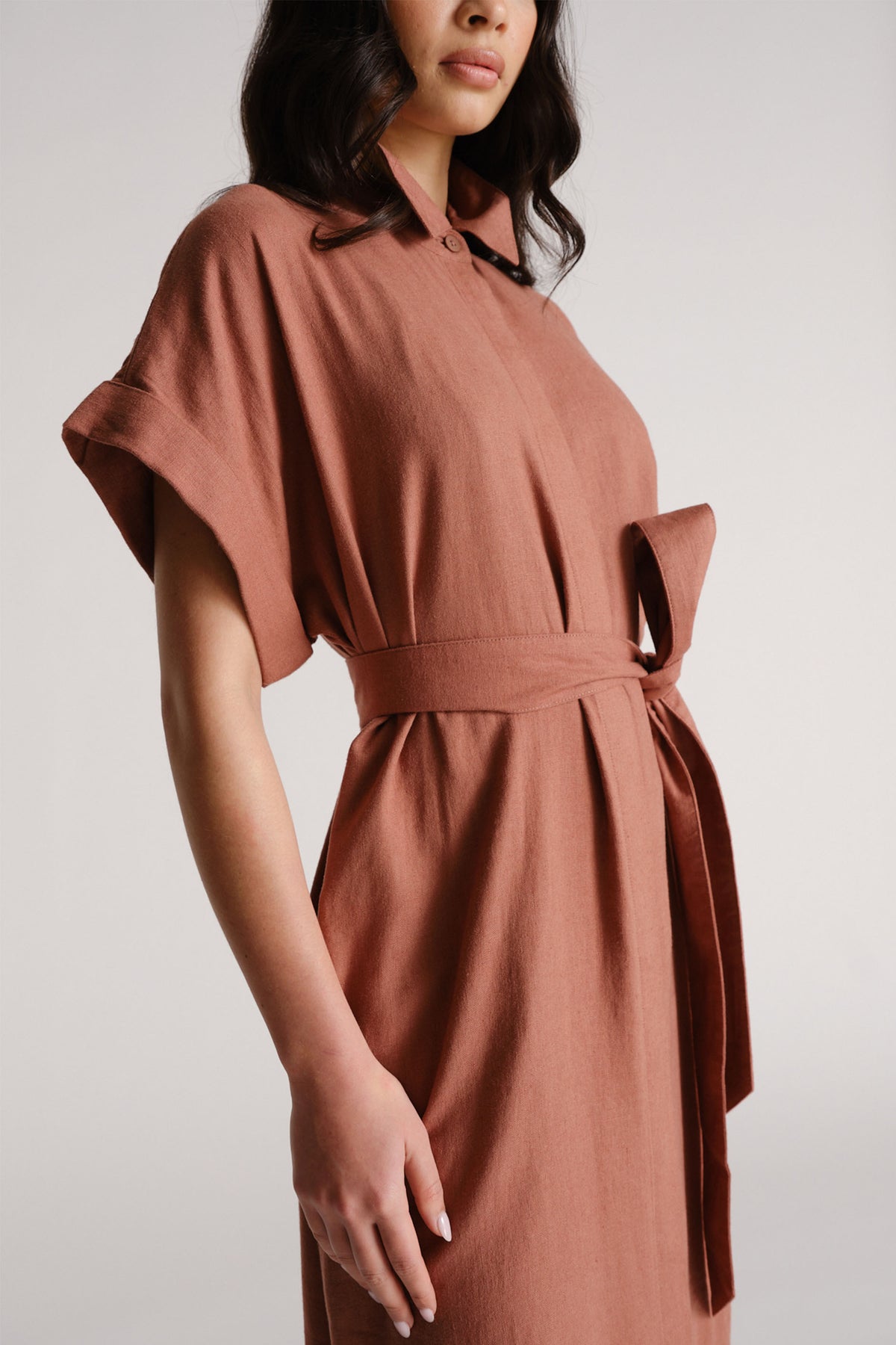 Woman wearing a rust-colored linen blend midi dress with a waist tie and relaxed short sleeves for effortless style