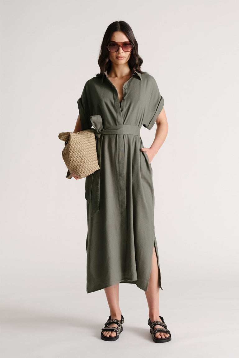 Portrait of woman wearing olive D-Luxe Linen Blend Midi Dress with belt, side slit, sandals, sunglasses, and woven bag
