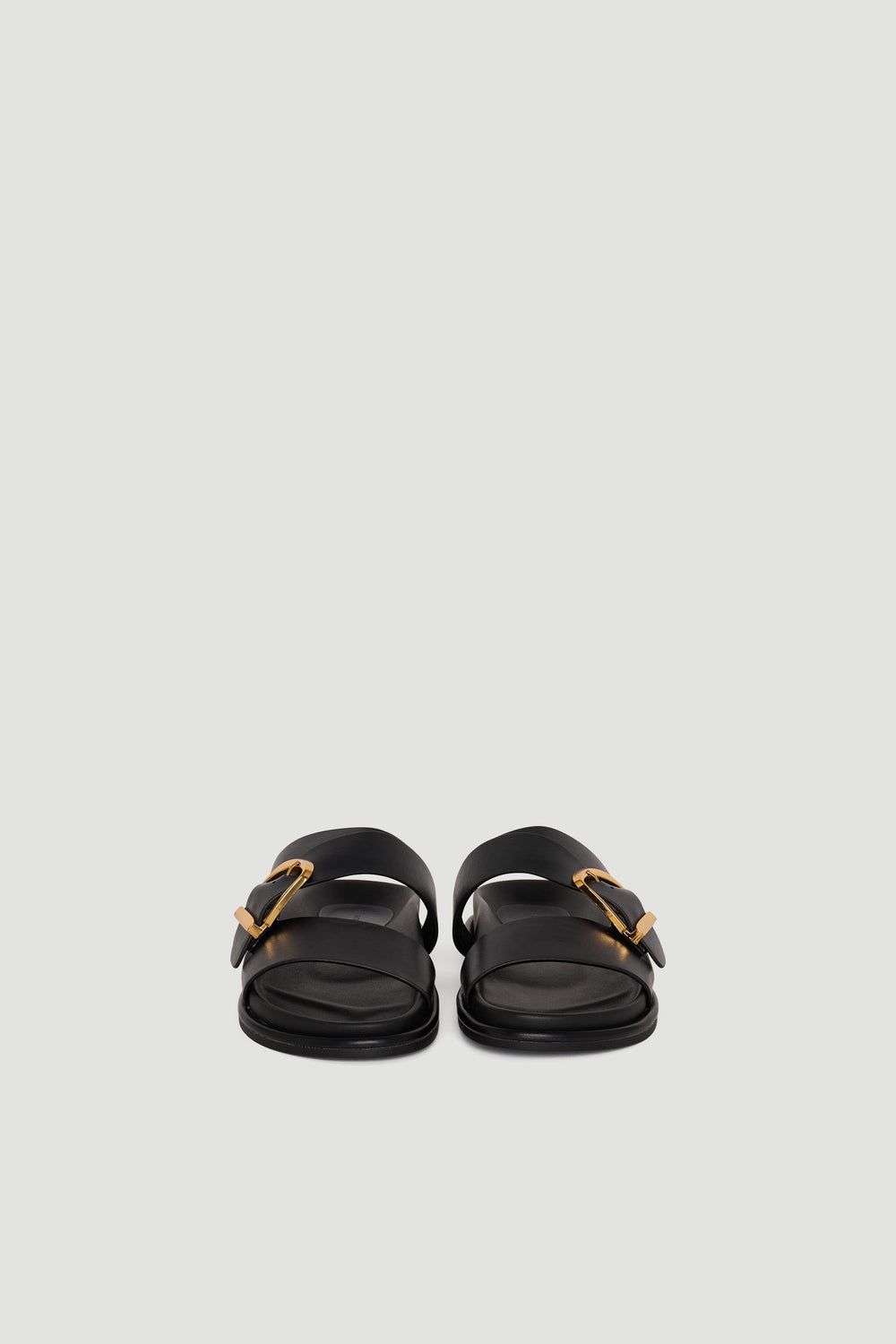 Pair of black slide sandals with wide straps and gold buckle accents on a plain background