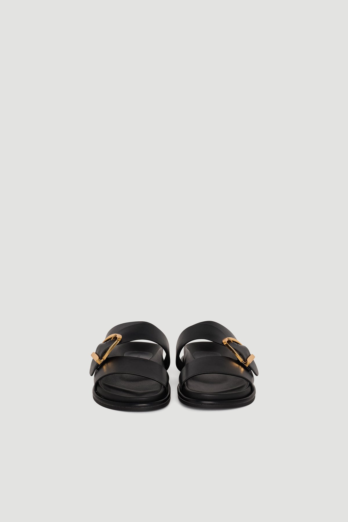 Pair of black slide sandals with wide straps and gold buckle accents on a plain background