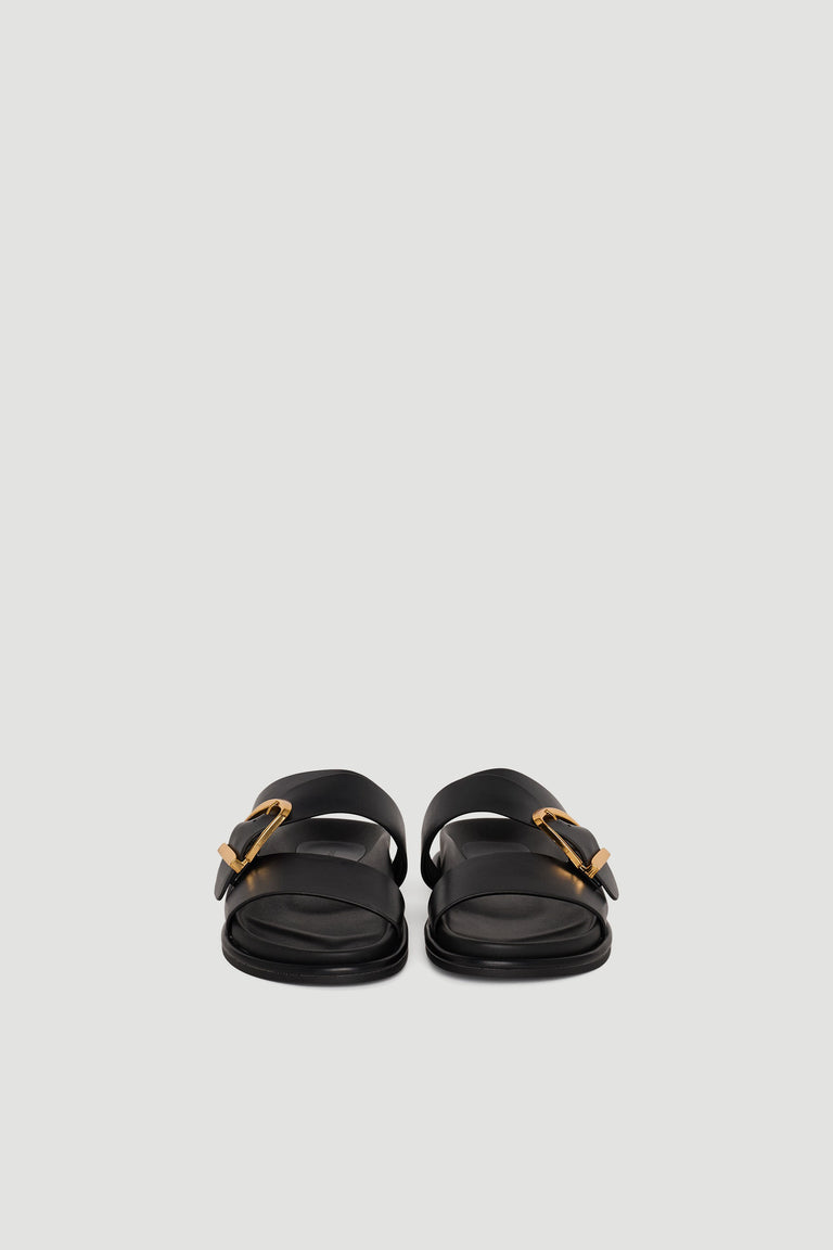 Pair of black slide sandals with wide straps and gold buckle accents on a plain background