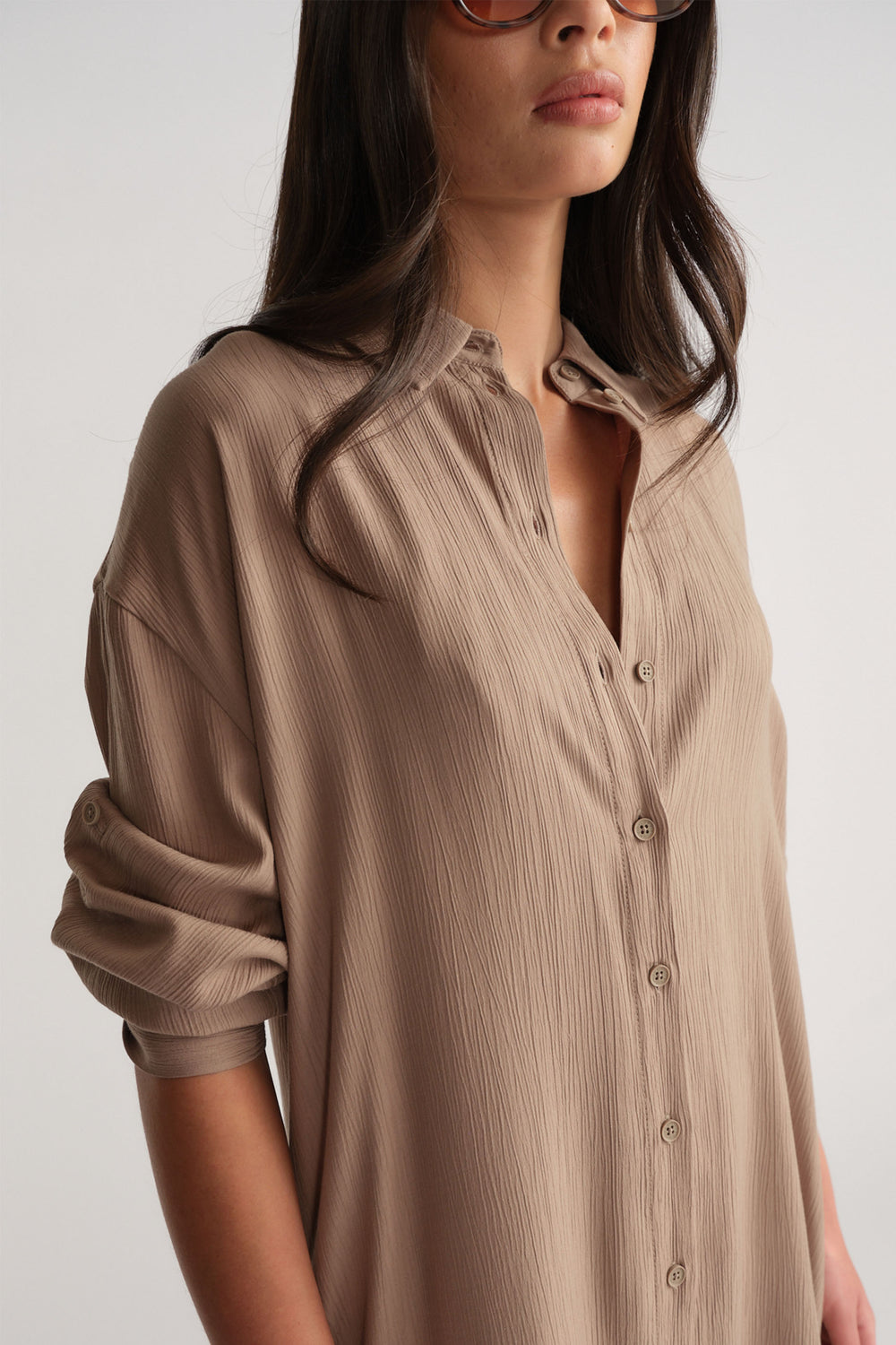 Close-up of a woman wearing a relaxed-fit textured shirt dress in a neutral barley tone with rolled sleeves and button details