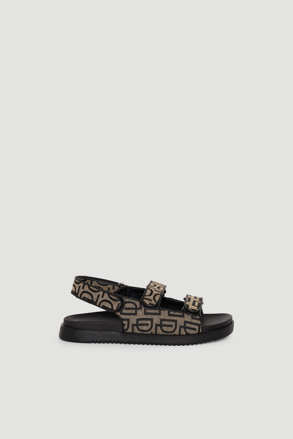 Sandal featuring black sole and adjustable straps with tan and black monogram pattern for casual, stylish wear.