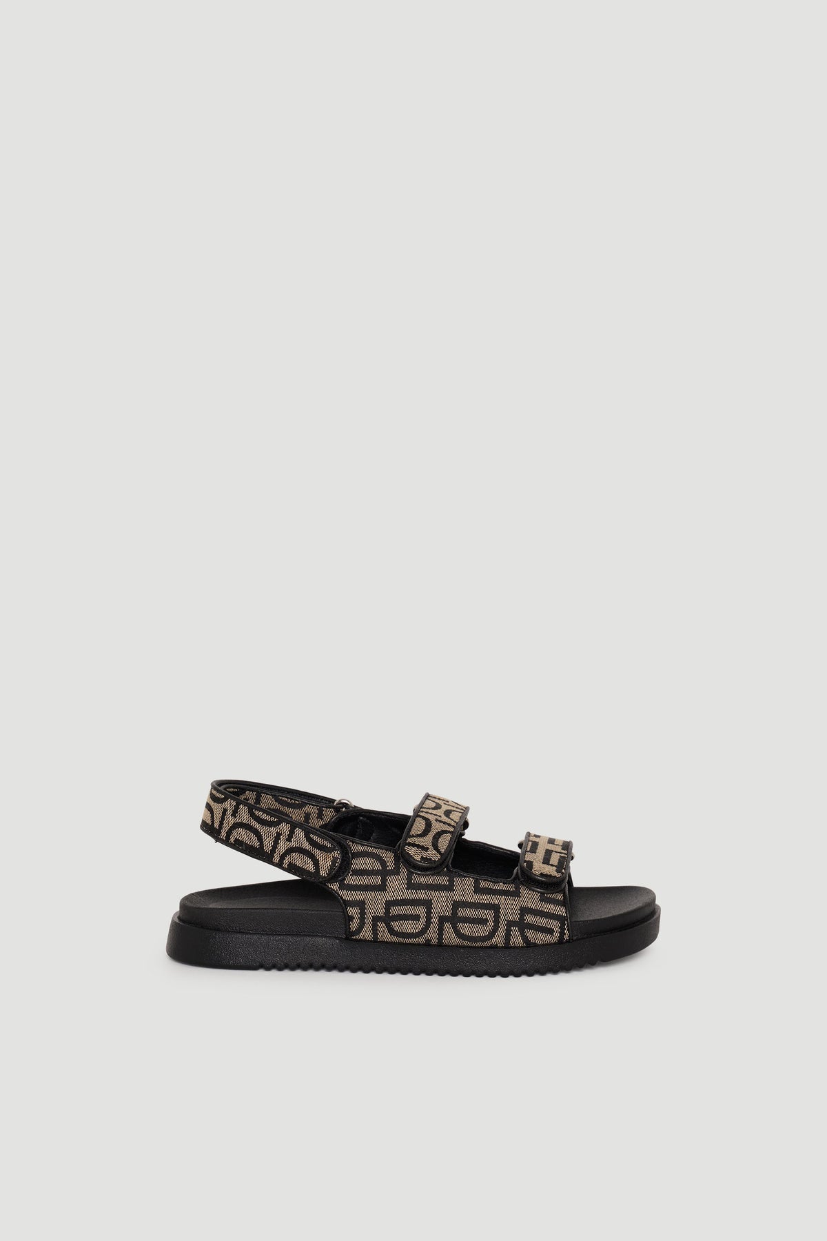 Sandal featuring black sole and adjustable straps with tan and black monogram pattern for casual, stylish wear.