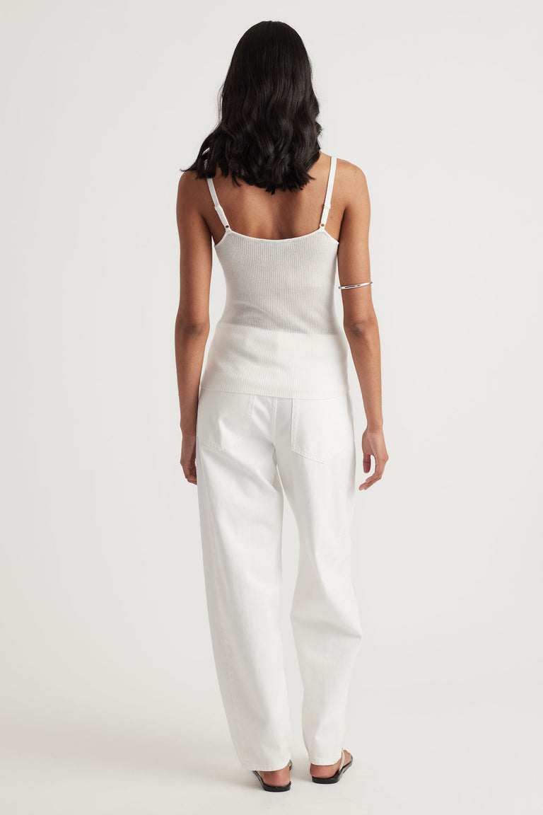 Woman wearing an ivory knit tank with adjustable straps paired with wide-leg white pants and black sandals, shown from the back.