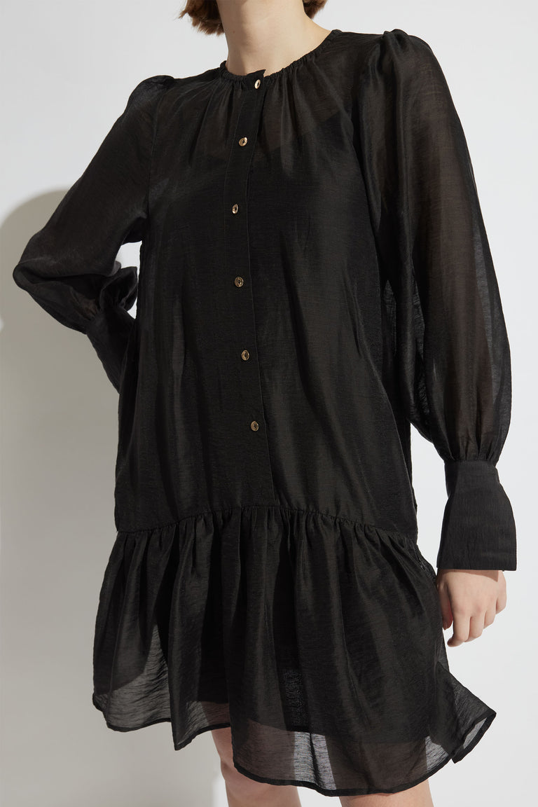 Woman wearing a black mini dress with gathered neckline balloon sleeves button front and drop waist