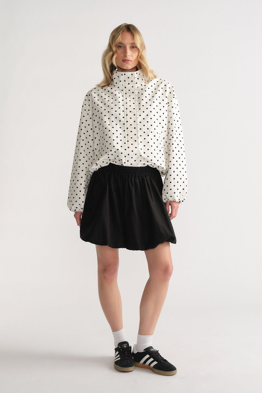 Woman wearing a polka dot zip-up jacket paired with a black bubble mini skirt and black sneakers with white socks