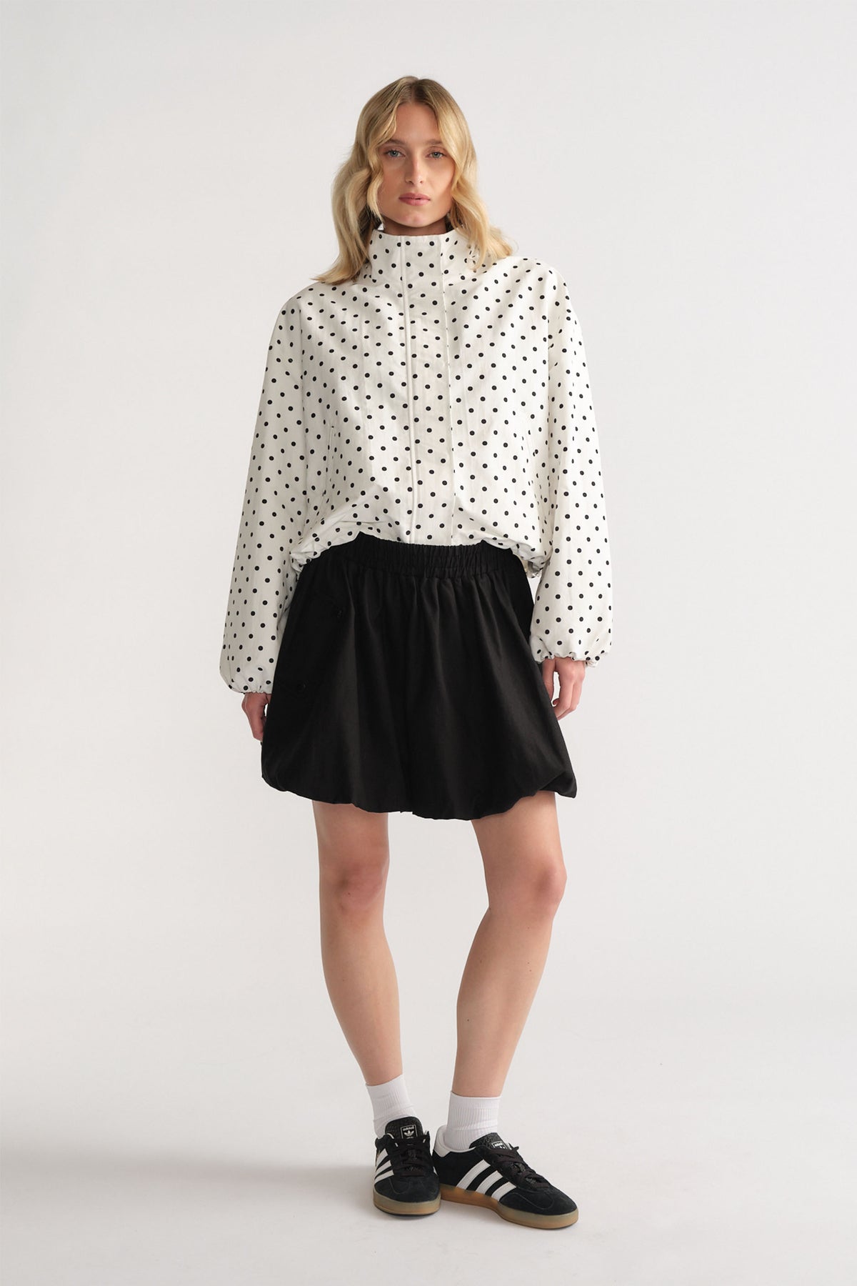 Woman wearing a polka dot zip-up jacket paired with a black bubble mini skirt and black sneakers with white socks