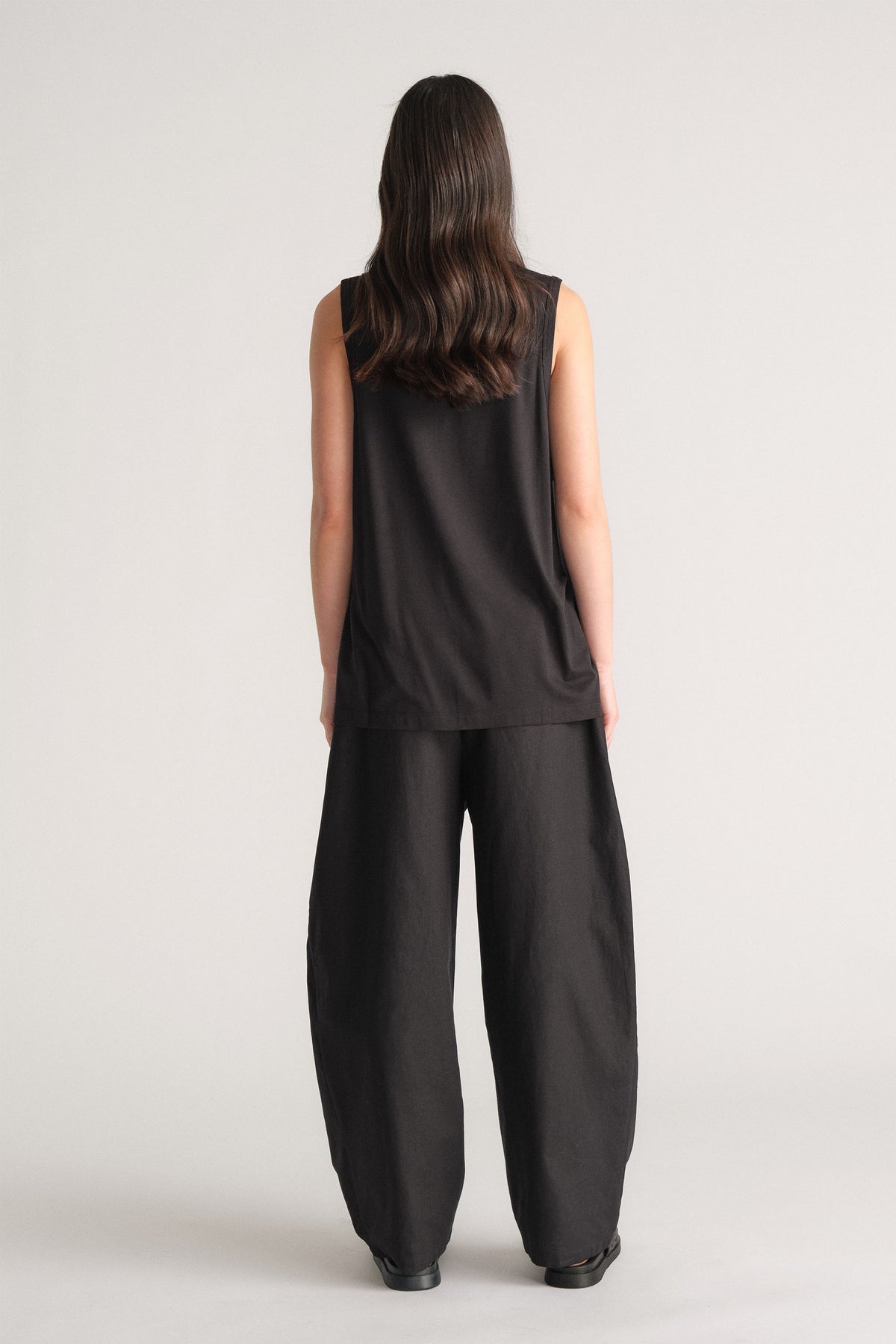 Woman wearing a relaxed black sleeveless tank paired with wide-leg black pants, standing against a neutral backdrop